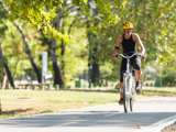 Woman wearing bike helmet riding e-bike on paved trail.